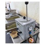 gray premelt tank on metal table with manual piston fully extended on top of the tank.